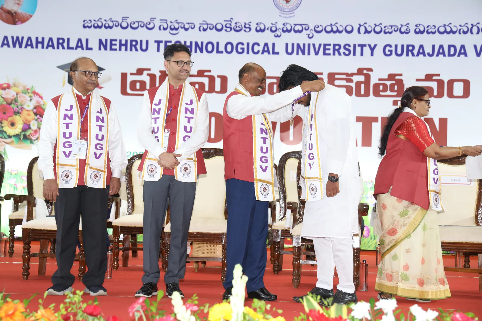 On the JNTUGV convocation stage: Prof. V. V. Subba Rao placing the gold medal around my neck, three other dignitaries in JNTUGV sashes standing beside us, the convocation banner behind